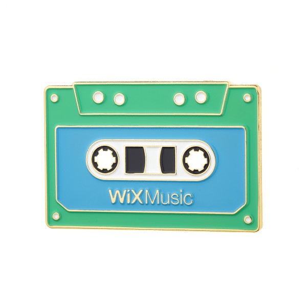 A greeny-blue soft enamel pin in the shape of a cassette that says