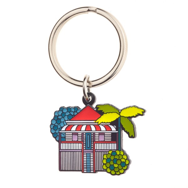 A soft enamel keychain in the shape of a red beach house surrounded by trees and flowers.